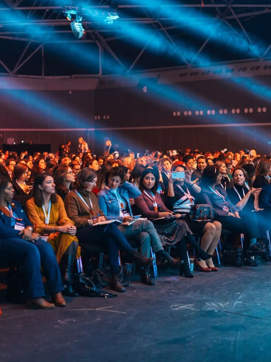 Plateia de evento corporativo sob iluminação de palco
